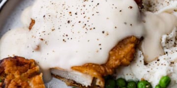 Closeup of country fried chicken covered with gravy and served with peas.